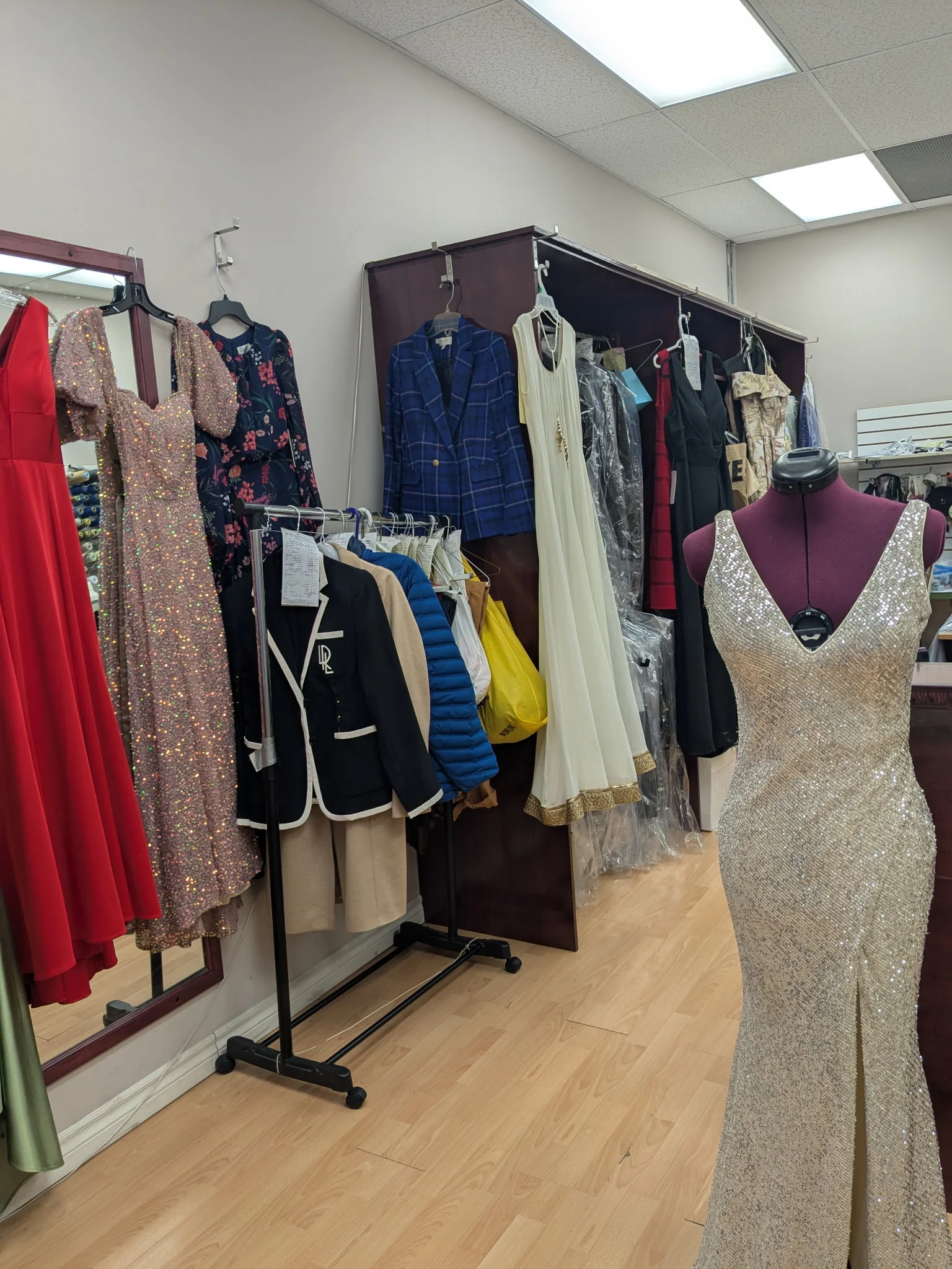 Collection of formal gowns and men’s suits on display inside Top Stitch tailoring shop.