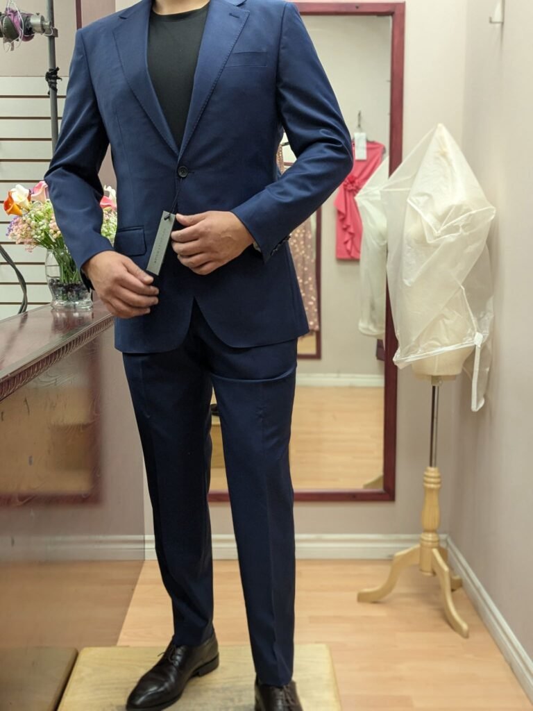 Man trying on tailored navy blue suit blazer at Top Stitch Mississauga with measurement tag during fitting appointment